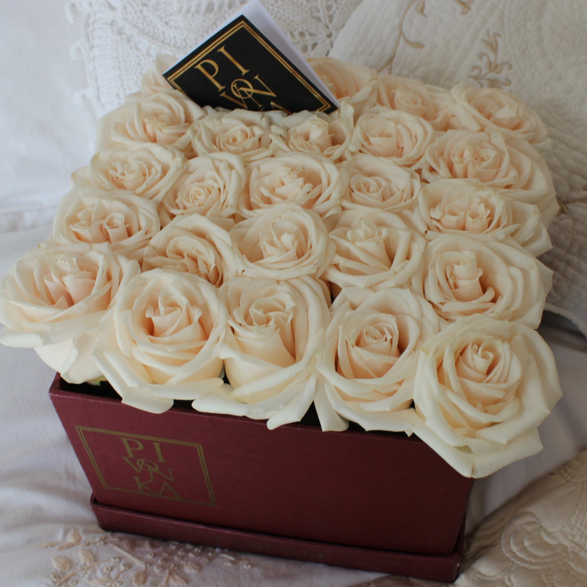 Pivonka Flores. Arreglo cuadrangular de 25 rosas blancas en base vino